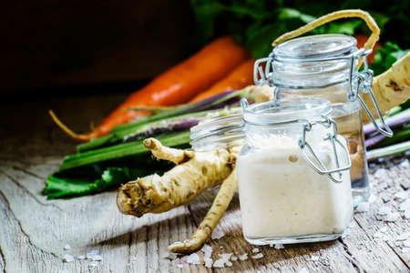 Grated horseradish in a glass jar, fresh root, vinegar and salt, vintage wooden background, selective focusの写真素材