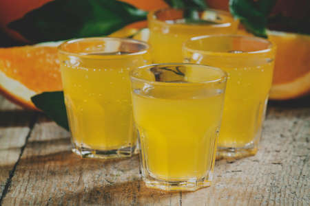 Orange soda on a background of fresh oranges on old wooden table, selective focus and toned image