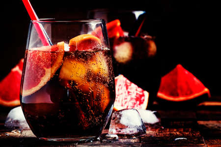 Cocktail with cola, grapefruit juice, ice cubes and liqueur, dark vintage wooden background,...