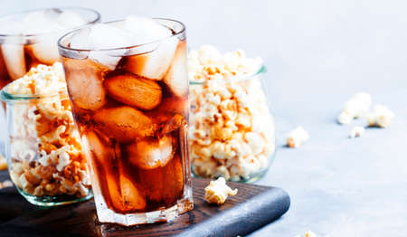 Sweet soda with ice cubes and caramel popcorn, gray background, selective focus