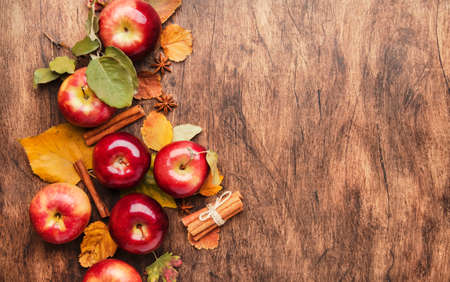 Autumn food background. Ripe apples with nuts, fallen leaves and cinnamon on rustic wooden table. Top view. Copy spaceの写真素材