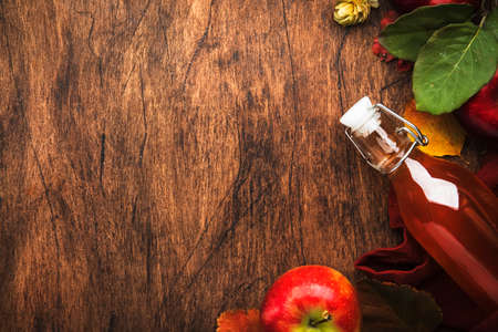 Apple cider vinegar. Bottle of fresh apple organic vinegar on wooden table background with cinnamon sticks, anise star, nuts and fallen leaves. Healthy organic food. Copy spaceの写真素材