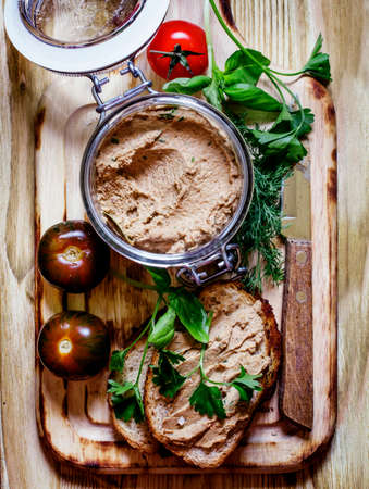 Homemade liver pate in a glass jar and fried toast, tomatoes and parsley, vintage wooden background,...