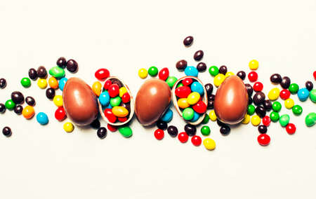 Easter composition with chocolate eggs and colorful candy, white background, top view