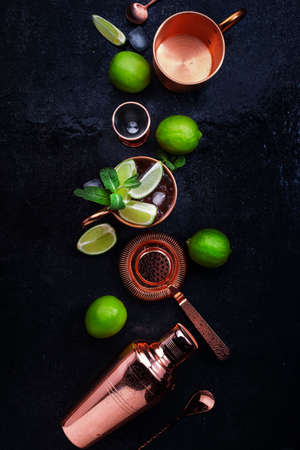 Preparation Moscow Mule cocktail with ginger beer, vodka, lime and ice. Copper bar tools. Black bar counter background. Top view. Copy spaceの写真素材
