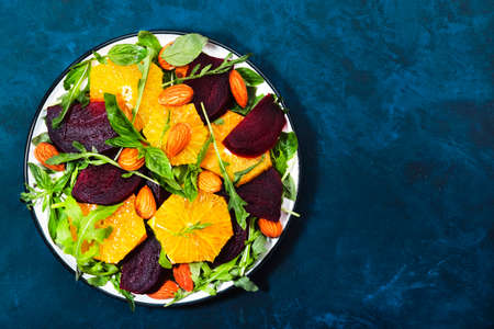 Fresh Beetroot Salad with Orange, arugula and almonds nut on blue background. Vegan healthy summer food. Flat lay. Copy spaceの写真素材