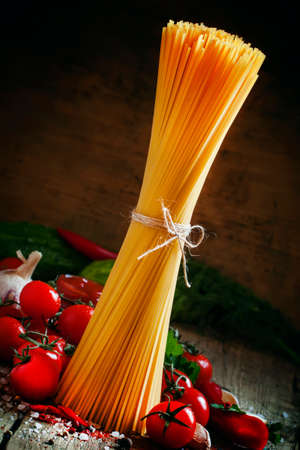 Italian dry pasta spaghetti with tomatoes and fresh herbs on a dark wooden background, selective focusの写真素材