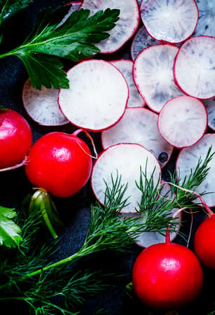 Sliced radish, parsley, dill, salt and spices on a dark background, food background, top view