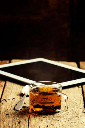 Cup of hot tea and tablet on old wooden table, selective focusの写真素材
