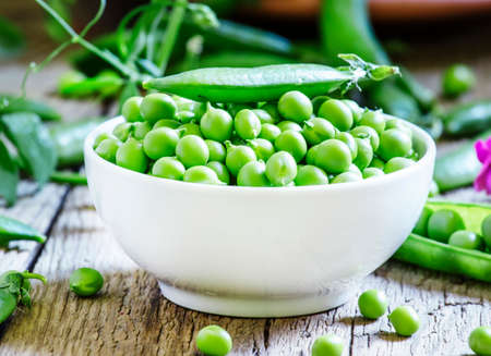 Peeled pea green peas in a white porcelain bowl, vintage wooden background, selective focusの写真素材
