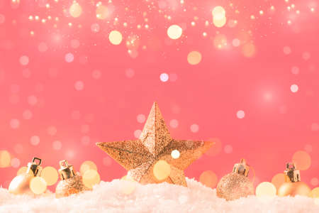 Christmas pink background with golden star. New Year's decor. Christmas balls in smowdrifts and golden bokeh lightsの写真素材