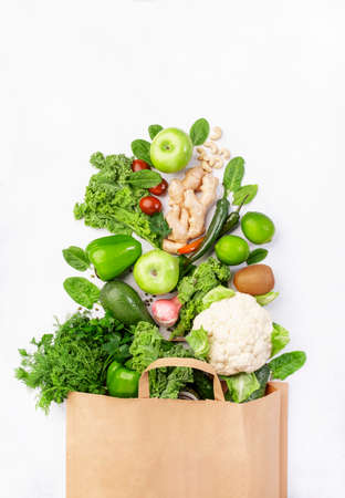 Healthy green vegan vegetarian food in full paper bag, vegetables and fruits on white background. Shopping food supermarket, raw detox diet and clean eating concept. Healthy food backgroundの写真素材