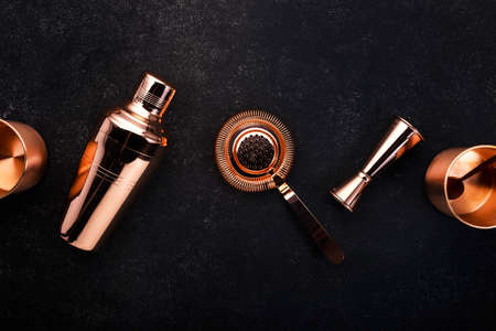 Copper bar tools and accessories for making cocktail. Shaker, jigger, strainer, spoon. Alcohol drinks and beverages preparation concept. Black background, top view, copy spaceの写真素材