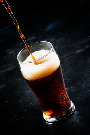Dark english beer, ale or stout is poured into glass, dark bar counter, space for text, selective...