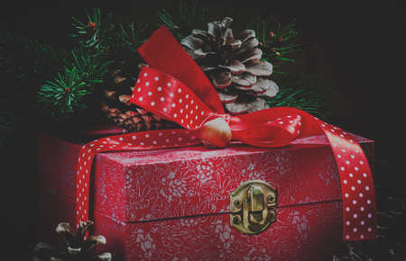 Holiday gift box decorated with red ribbon, pine cones, fir branches, Christmas balls and nuts, toned image, selective focus and toned imageの写真素材