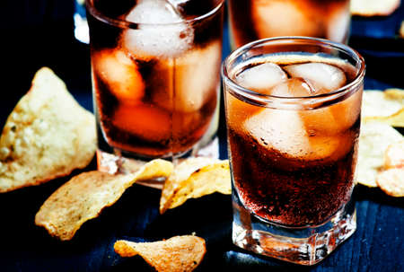 Cold Cola with ice in glasses and potato chips on a dark background, unhealthy eating habits,...