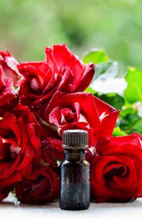 Essential rose oil in a brown glass bottle, bouquet of red roses, natural background, selective focusの写真素材
