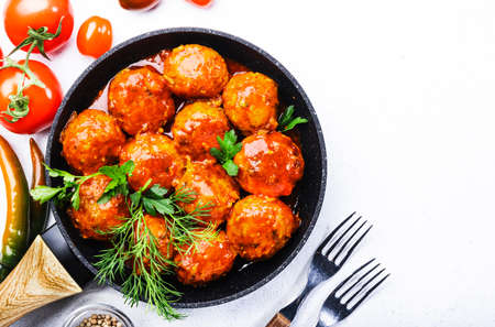 Meatballs with tomato sauce and spices in frying pan on white kitchen table background. Top view with copy spaceの写真素材