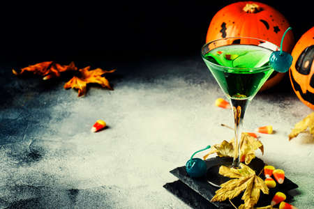 Halloween composition with festive drink, green cocktail and pumpkins lanterns, smoke and fallen leaves on night dark blue background, selective focusの写真素材