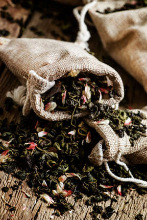 Dry green tea with petals of cherry, vintage wooden background, selective focus