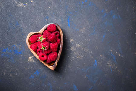 Fresh raspberries in a bowl in the shape of a heart on a dark background, top view