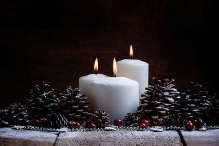 White burning candle with pine cones and cranberries, Christmas or New Year background with the drawn snow, selective focusの写真素材