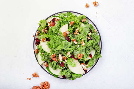 Kale salad with dried cranberry, green apples and walnuts. Healthy vegan food, top view, gray...