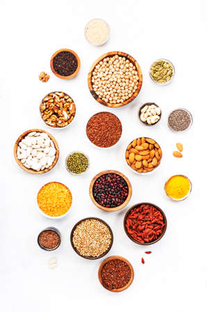 Various superfoods, legumes, cereals, nuts, seeds in bowls on white background. Superfood as chia, spirulina, beans, goji berries, quinoa, turmeric, mung bean, buckwheat, lentils, flax seed, wild rice and almond. Copy space, top viewの写真素材
