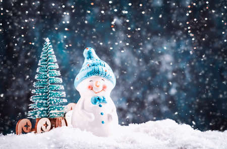 Merry Christmas and happy New Year composition with copy space. Little snowman carries Christmas tree from fairy forest to home. Winter festive background
