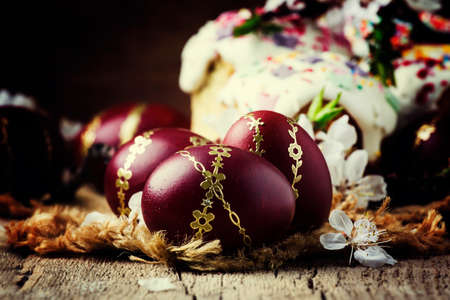 Easter red and burgundy eggs with gold pattern, white apricot flowers, festive composition in rustic...