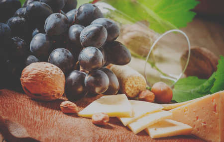 Cheese, blue grapes, vine, nuts and a glass, selective focus and toned imageの写真素材