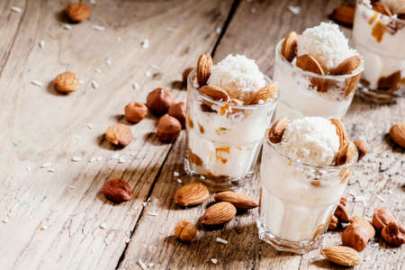 Dessert with vanilla ice cream, nut sauce, almonds, hazelnuts and coconut, served in glasses,...