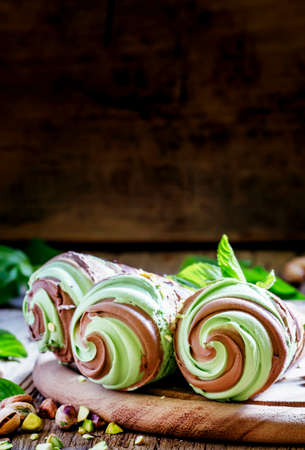 Green pistachio ice cream with chocolate and mint in cones, vintage wooden background, selective focusの写真素材