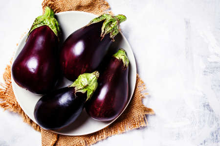 Fresh purple eggplants on plate, top viewの写真素材