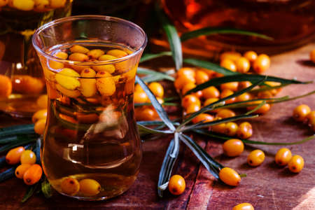 Curative tea with sea-buckthorn berries in oriental glasses, dark wood background, selective focus
