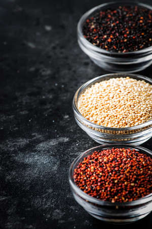 Black, white and red quinoa in bowls, raw quinoa groats set on gray kitchen table, copy space, selective focusの写真素材