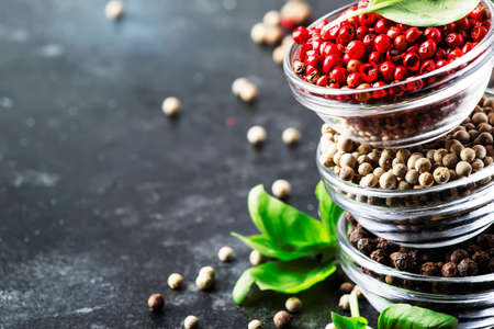 Black, white and pink rose peppers in bowls, assorted spices on gray kitchen table, selective focusの写真素材