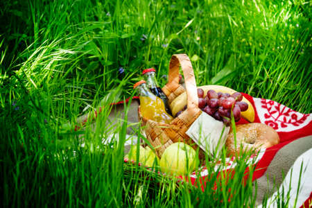 Picnic Basket with fruits and drinks on the meadow on a background of green spring grass, selective focusの写真素材