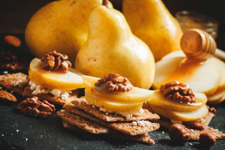 Appetizer from crispy dark breads, cottage cheese, walnuts and pears with honey, dark background, selective focusの写真素材