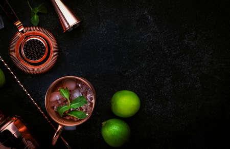 Preparation Moscow Mule cocktail with ginger beer, vodka, lime and ice. Copper bar tools. Black bar counter background. Top view. Copy spaceの写真素材