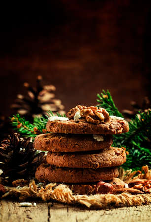 Christmas chocolate cookies with nuts, fir branches, pine cones and snowflakes, vintage wood background, selective focusの写真素材