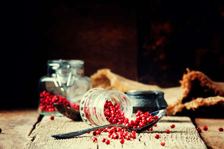 Pink pepper in spoon and jar on vintage wooden background, selective focusの写真素材