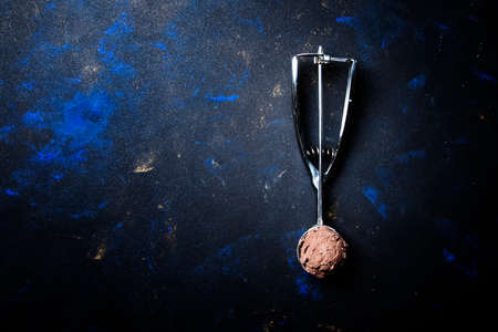 Chocolate ice cream in metal spoon for ice cream, dark background, top view