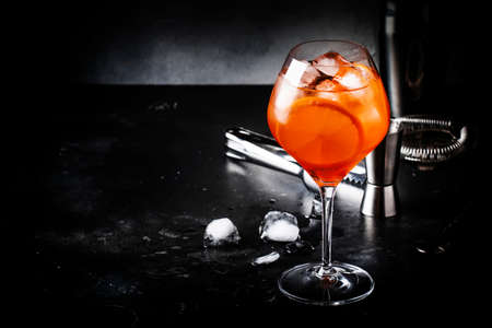 Aperol spritz cocktail in big wine glass with orange and ice, summer alcoholic cold drink, dark bar...