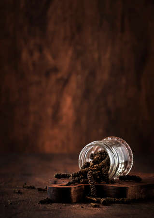 Fragrant long pepper spilling out of glass jar, vintage kitchen table background, selective focusの写真素材