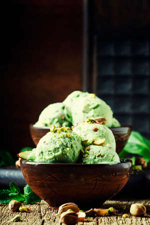 Pistachio ice cream with nuts, decorated with mint leaves, vintage wooden background, selective focusの写真素材