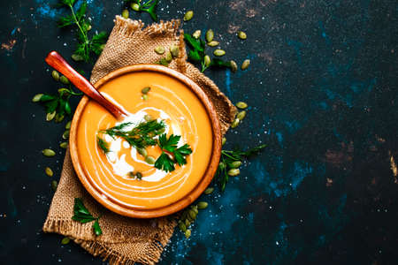 Creamy pumpkin soup in a wooden bowl, blue background, top view