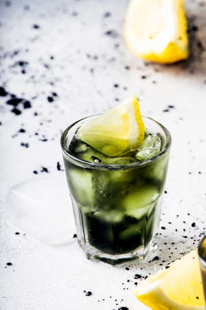 Healthy food and drink concept: iced black detox mineral water with crushed ice and lemon slices in glasses, activated charcoal, gray background, trendy beverage, selective focusの写真素材