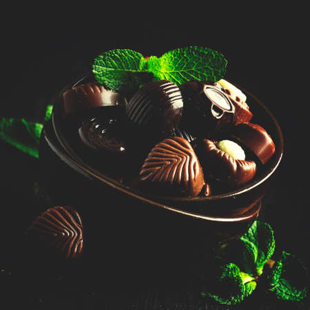 Chocolate candies, assorted, decorated with mint leaves, dark background, low key, selective focus and toned imageの写真素材