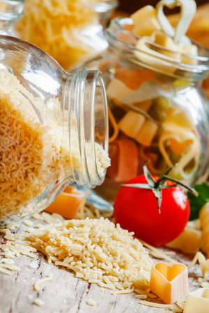 Dry Italian pasta alpfabeto in the form of letters of the alphabet in a glass jar, mix of different types of pasta, parsley and tomatoes on old wooden background, selective focusの写真素材